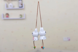 Detail of two white ceramic rabbit wind chimes with colorful beads and hanging strings