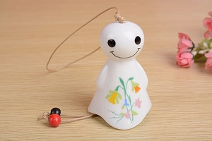 Detail of a white ceramic sun doll wind chime with floral patterns and wooden beads