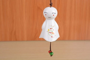Detail of a white ceramic sun doll wind chime with floral pattern and woven rope
