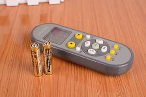 Detail view of a dark grey AC remote control paired with two gold 1.5V AAA batteries