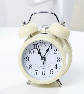 Detail view of cream-colored twin bell alarm clock with quartz movement and metal legs