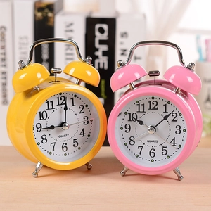Minimalist round twin bell alarm clocks in pink and yellow on wooden table