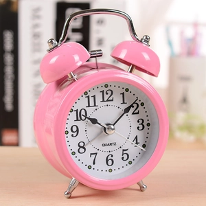 Classic pink metal twin bell quartz alarm clock for kids on a cozy desk setting