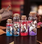 Detail view of four glass wishing bottles with colorful sand, shells and cork stoppers