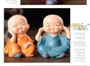 Detail of two cute resin little monk figurines in orange and blue robes laughing