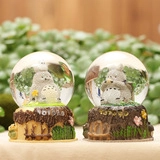 Detail of two Totoro themed crystal balls with decorative floral bases in a forest setting