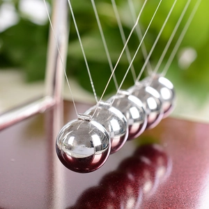 Pendolo di Newton classico con sfere di metallo argento su base rosso scuro in giardino