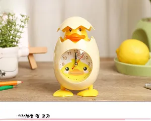 Close-up of a cartoon chick alarm clock on a desk with pencils and a lemon