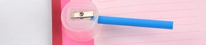 Close-up of a manual pencil sharpener in use with a blue pencil on a pink notebook