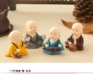 Set of four colorful resin monk figurines in zen setting with tea and pine cones