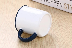 Close-up of white ceramic mug with blue rim and handle on a light wood background