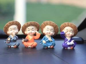Close-up of four resin monks in colorful robes with straw hats on a car dashboard