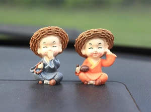 Detail of two resin monk car ornaments wearing woven straw hats on a dashboard