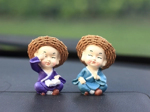 Detail of two monk figurines with straw hats and textured robes for car dashboard decoration