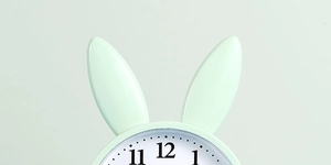 Close-up of a minimalist light green rabbit alarm clock with cute ears and clear dial