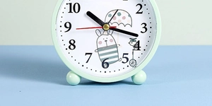 Close-up of mint green alarm clock with cute rabbit illustration on a round dial