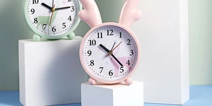 Close-up of pink round alarm clock with cute reindeer antlers on geometric pedestal
