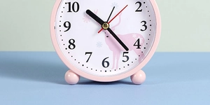Close-up of pink round alarm clock featuring cartoon deer illustration and black numerals