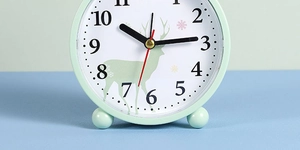 Close-up of mint green round alarm clock with elk pattern and clear Arabic numerals