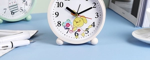 Close-up of a white cartoon rabbit alarm clock on a desk with books and coffee