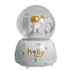 Astronaut snow globe music box featuring moon model and gold hello letters on white base