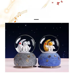 Astronaut snow globe music boxes with silver and gold moon themes on lunar textured bases