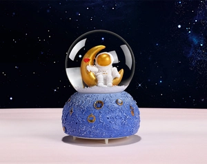 Detailed view of astronaut sitting on a gold moon inside a crystal music box