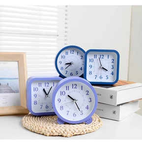 Detail of round and square analog alarm clocks in lavender and deep blue on a wooden desk