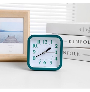 Minimalist square alarm clock in dark teal finish on a bright desk with natural lighting
