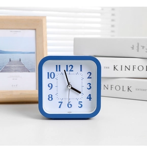 Detail view of a blue square analog alarm clock with clear numerals on a home desk