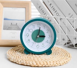 Detailopname van een minimalistische stille tafelklok in donkergroen op een houten bureau