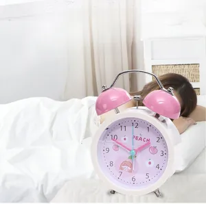 Close-up of pink silent alarm clock with cartoon peach dial and metal twin bell design