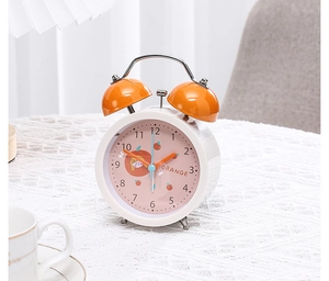 Close-up of orange twin bell alarm clock with cartoon orange dial on white lace tablecloth