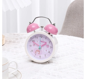 Detail of cartoon twin bell alarm clock featuring peach illustration on white lace tablecloth