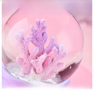 Macro detail of a crystal ball music box featuring pink coral and a purple resin base