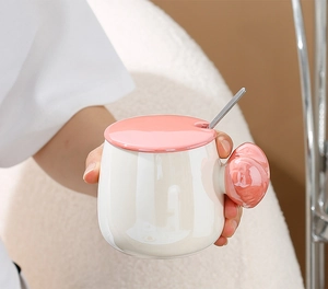 Close-up of pearl glaze ceramic mug with spherical handle and matching pink lid and spoon