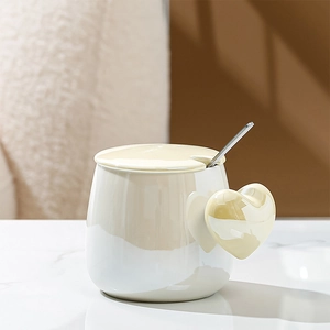 Detailed close-up of cream white ceramic heart handle mug with matching lid and silver spoon