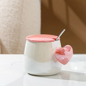 Detail of ceramic mug with pink heart-shaped handle, matching lid and silver mixing spoon