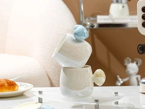 Detail of ceramic mugs with heart-shaped handles and pearl glaze stacked on a tray