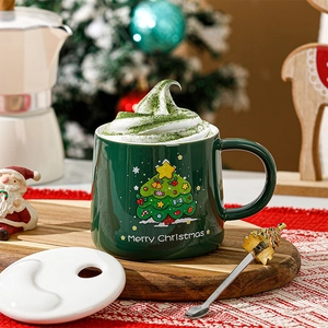 Détail d'un mug de Noël en céramique vert foncé avec couvercle blanc et cuillère dorée