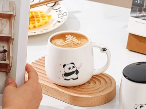 Dettaglio di una tazza in ceramica panda con manico a zampa di gatto su base in legno