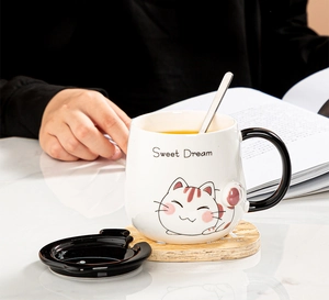 Detail of white ceramic cat mug with black lid and long metal spoon on marble surface