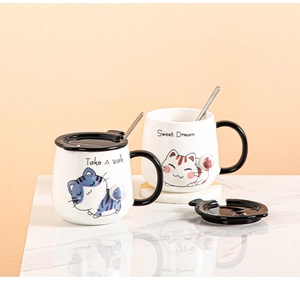 Detail of cartoon cat ceramic mugs with 3D paw lids and spoons on marble surface