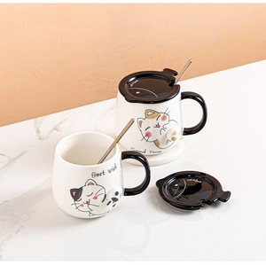 Detail of white ceramic cat mugs with black lids and stainless steel mixing spoons