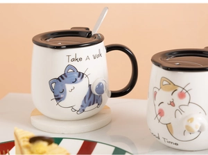 Close-up of white ceramic cat mug with spoon, lid and cute hand-painted illustrations