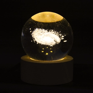 Macro shot of 3D laser-engraved galaxy inside a crystal ball with a warm wooden base
