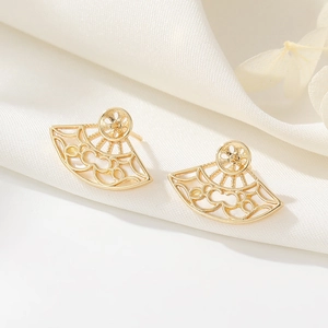 Macro detail of 14K gold openwork fan-shaped stud earrings on white silk fabric background