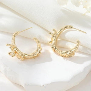 Detalle de pendientes de aro chapados en oro de 14K con textura sobre base de piedra