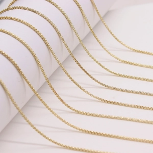 Multiple strands of shiny gold box chains arranged on a minimalist white pedestal