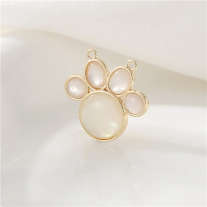 Detail of a 14K gold-plated cat paw charm with a white shell inlay and dual loop rings